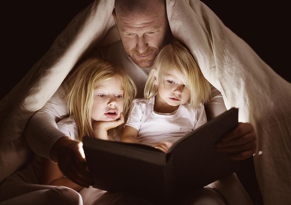 A man reading with two children under a blanket A man reading with two children under a blanket