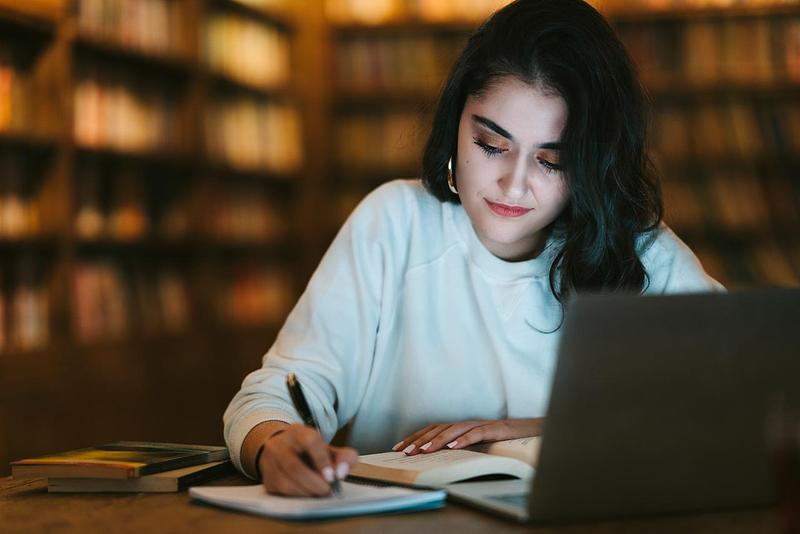 Young person writing at desk surrounded by bookshelves