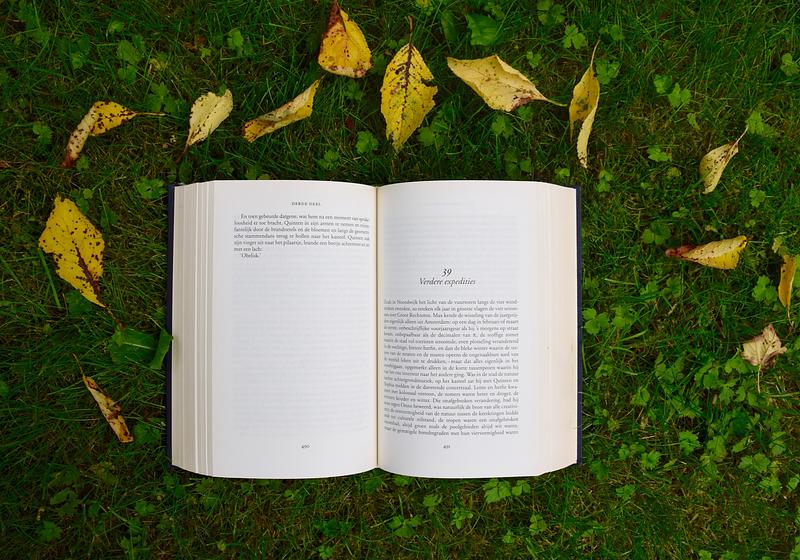 Open book on green grass in nature, surrounded by fallen leaves