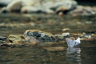 Small paper boat in water beside some rocks