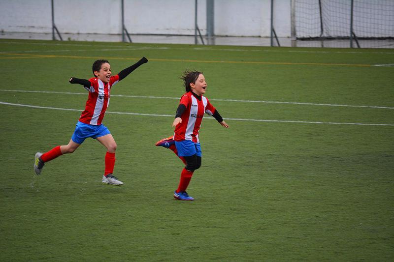 Two children in red and white football shirts and red shorts celebrating a goal
