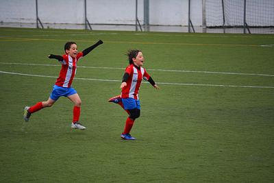 Two children in red and white football shirts and red shorts celebrating a goal