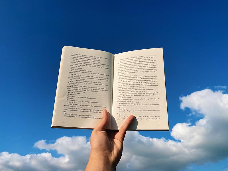 Open book being held up to blue sky with clouds