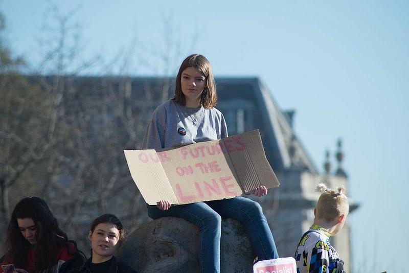 Young woman with cardboard sign reading 'Our Future's On The Line'