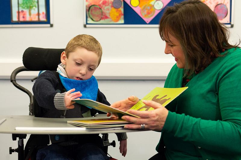 A child reading a picture book with a woman