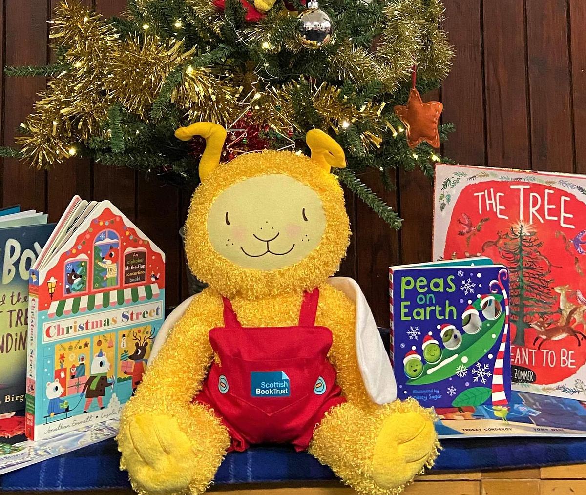 Large Bookbug doll sat amongst festive books underneath a Christmas tree