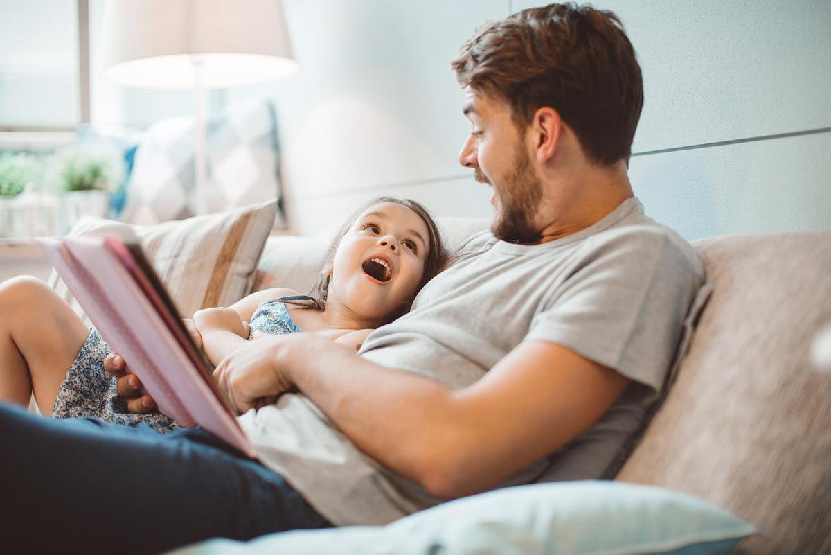 Father and daughter reading a book together, looking at each  other with surprised, happy expressions