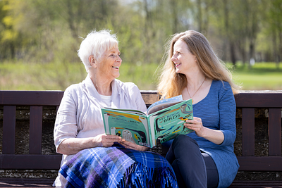 Mother and daughter reading a book together on park bench