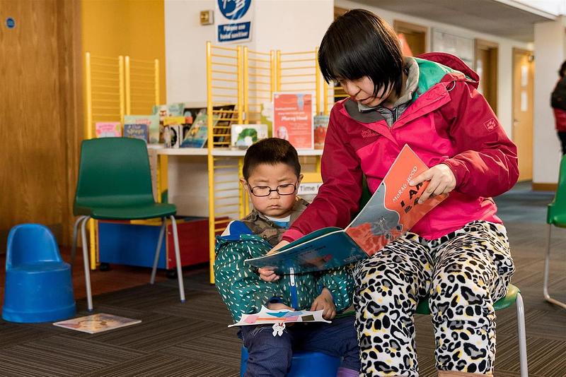 Image of young boy reading with his mother in a library during a storytelling session