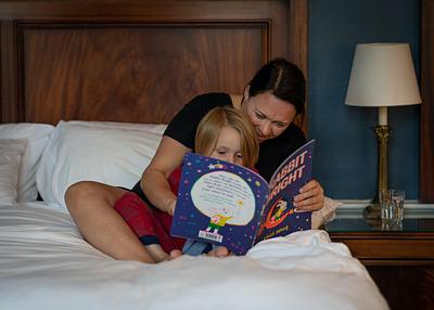 A mum and little boy reading a picture book together on a bed