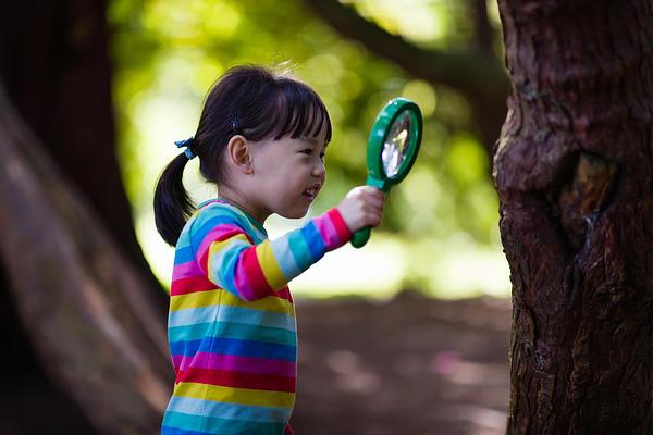 Child inspecting a tree with a magnifying glass, with a smile on her face