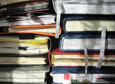 A messy pile of notebooks with pens, ribbons and bookmarks tucked inside