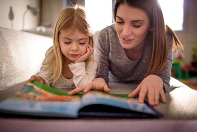 Mother and daughter lying on their stomachs, reading a picture book together