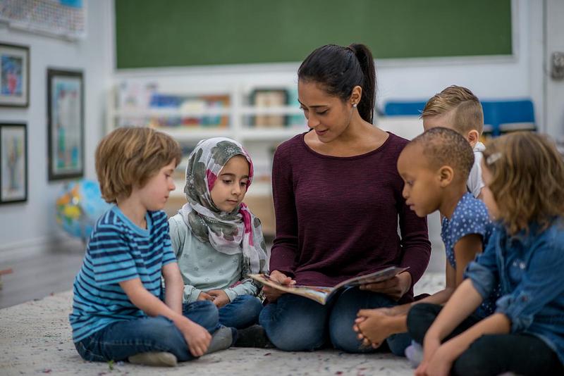 Children and teacher or nursery practitioner sat together reading a book