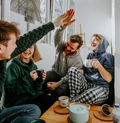 Four friends sitting around a table drinking coffee in comfortable clothing, two of them high-fiving