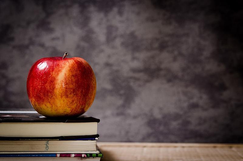 An apple on a pile of books with a blackboard in the background