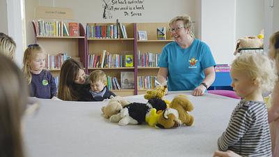 Bookbug Session in a library, featuring a Bookbug Session Leader holding the edges of lycra with teddies on it