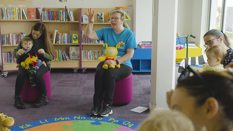 Bookbug Session leader holding a Bookbug Session in a library with families sat on the floor