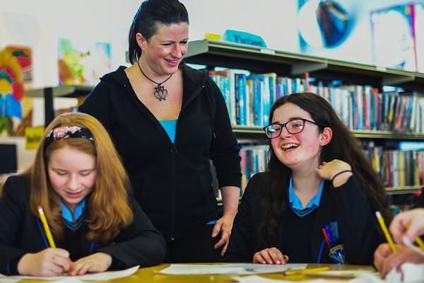 Two pupils writing at a table and laughing with a visiting author in the library