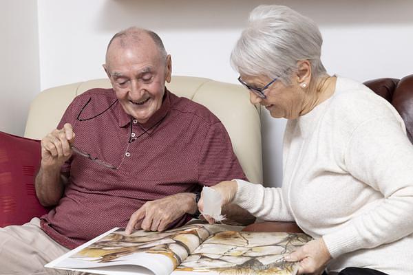 A elderly woman looking at a book with her husband