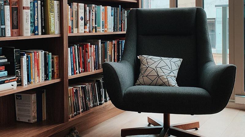 Gray fabric padded rolling armchair near bookshelves