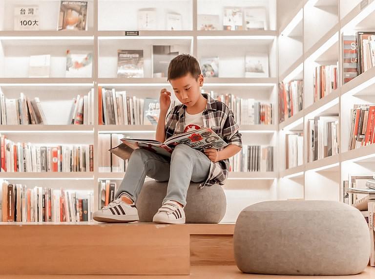 Child sat reading a book, surrounded by book shelves