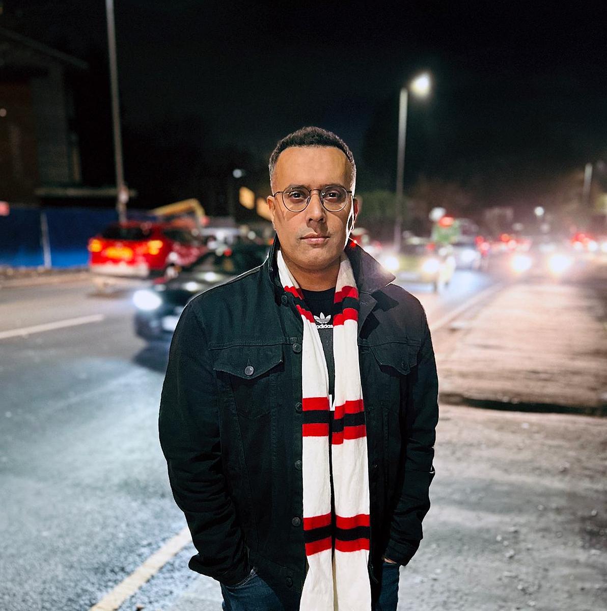 Nooruddean Choudry standing by a busy road at night, wearing a striped football scarf