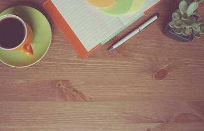 Notebook beside coffee, pen and pot plant on a desk