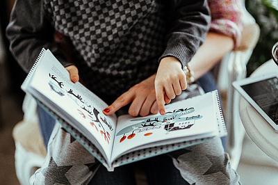 Child reading picture book with adult, pointing to pictures