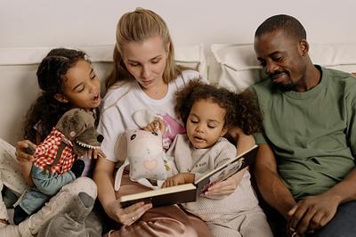Family of mum, dad and two children reading a book together on a sofa