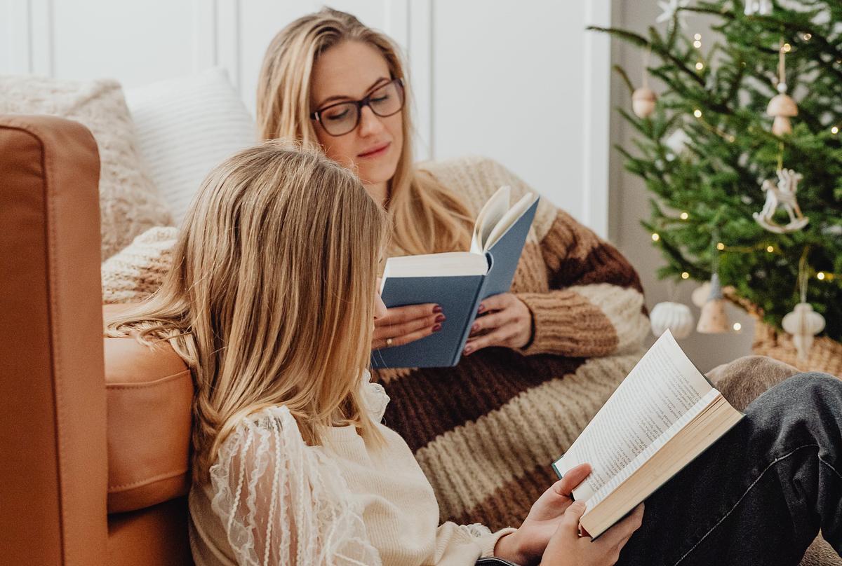 Woman and girl reading side by side next to a christmas tree