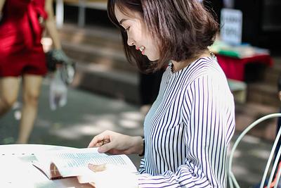 Woman reads book sitting at table outside in sunlight