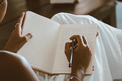 Person writing in notebook on white sheet