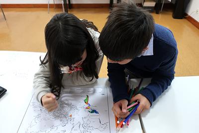 Two children in school uniforms colour in map of world