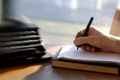 Slightly blurry image of person writing on notepad next to typewriter