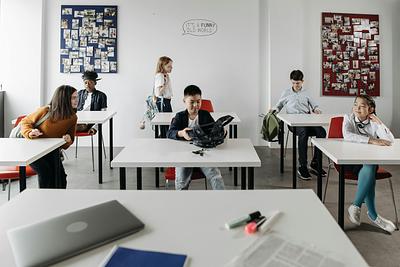 Children sit at white desks in classroom with noticeboards behind them